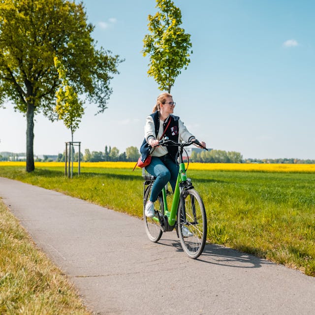 Frau fährt auf einem Fahrrad zwischen Wiesen hindurch