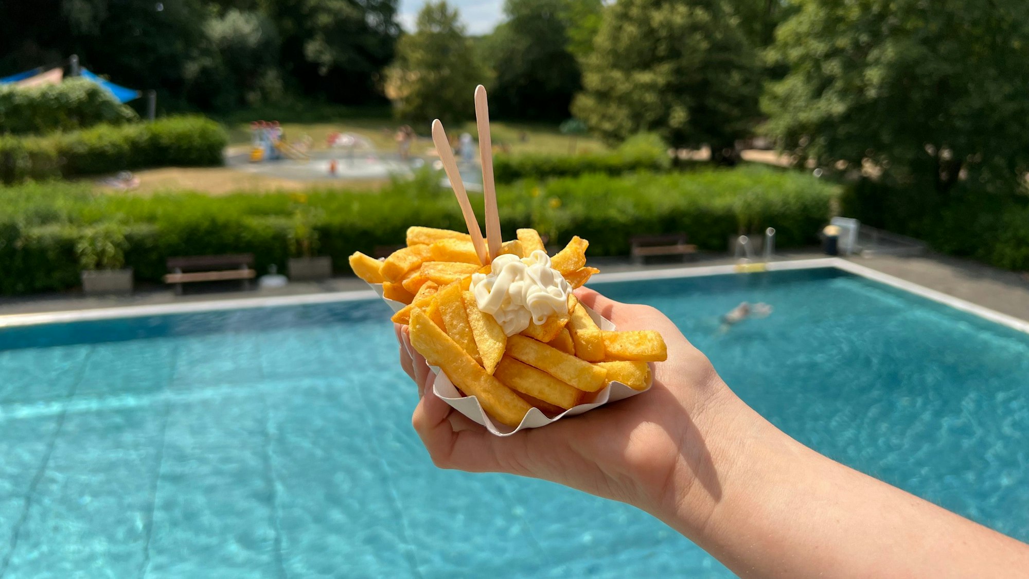 Eine Schale Pommes mit Mayo ist vor einem Schwimmbecken zu sehen.