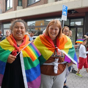 Zwei junge Frauen haben sich Regenbogenfahnen umgehangen. Eine von ihnen schwenkt zusätzlich eine Regenbogenflagge.