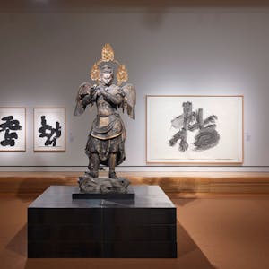 Die Skulptur eines flötenden Gottes steht von Zen-Gemälden mit schwarzen Schriftzeichen auf weißem Grund.