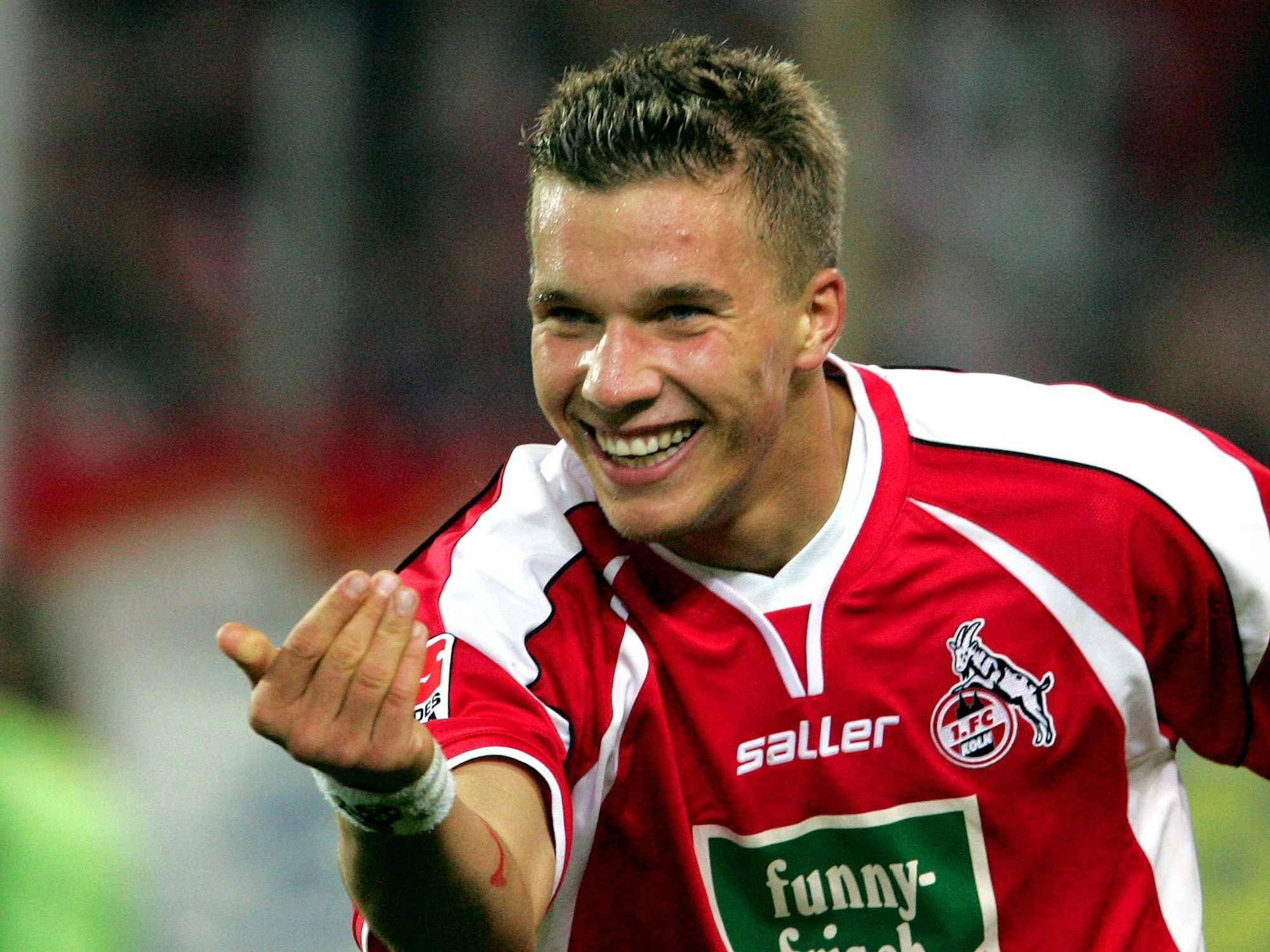 Lukas Podolski winkt einen Mitspieler mit der Hand herbei und grinst.