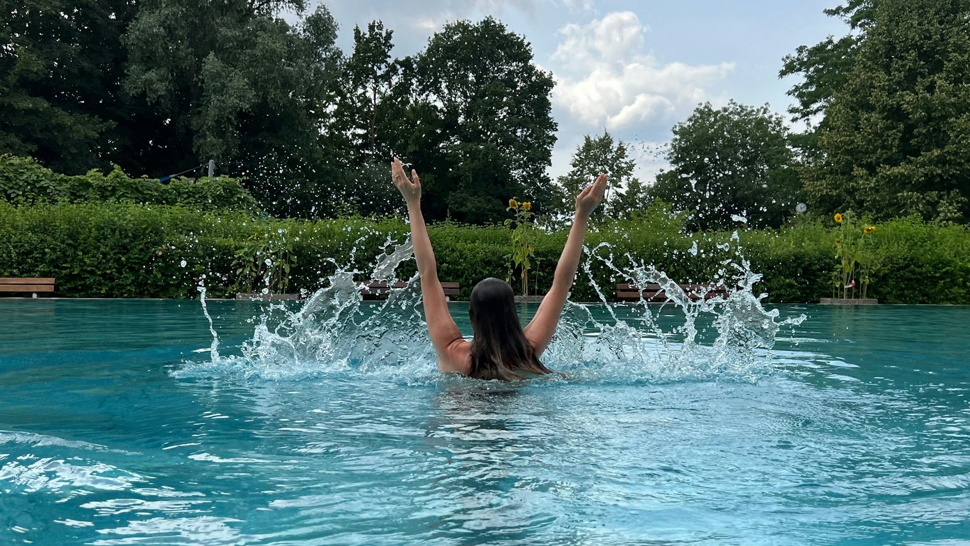 Eine junge Frau reckt im Schwimmbecken die Arme in die Luft.