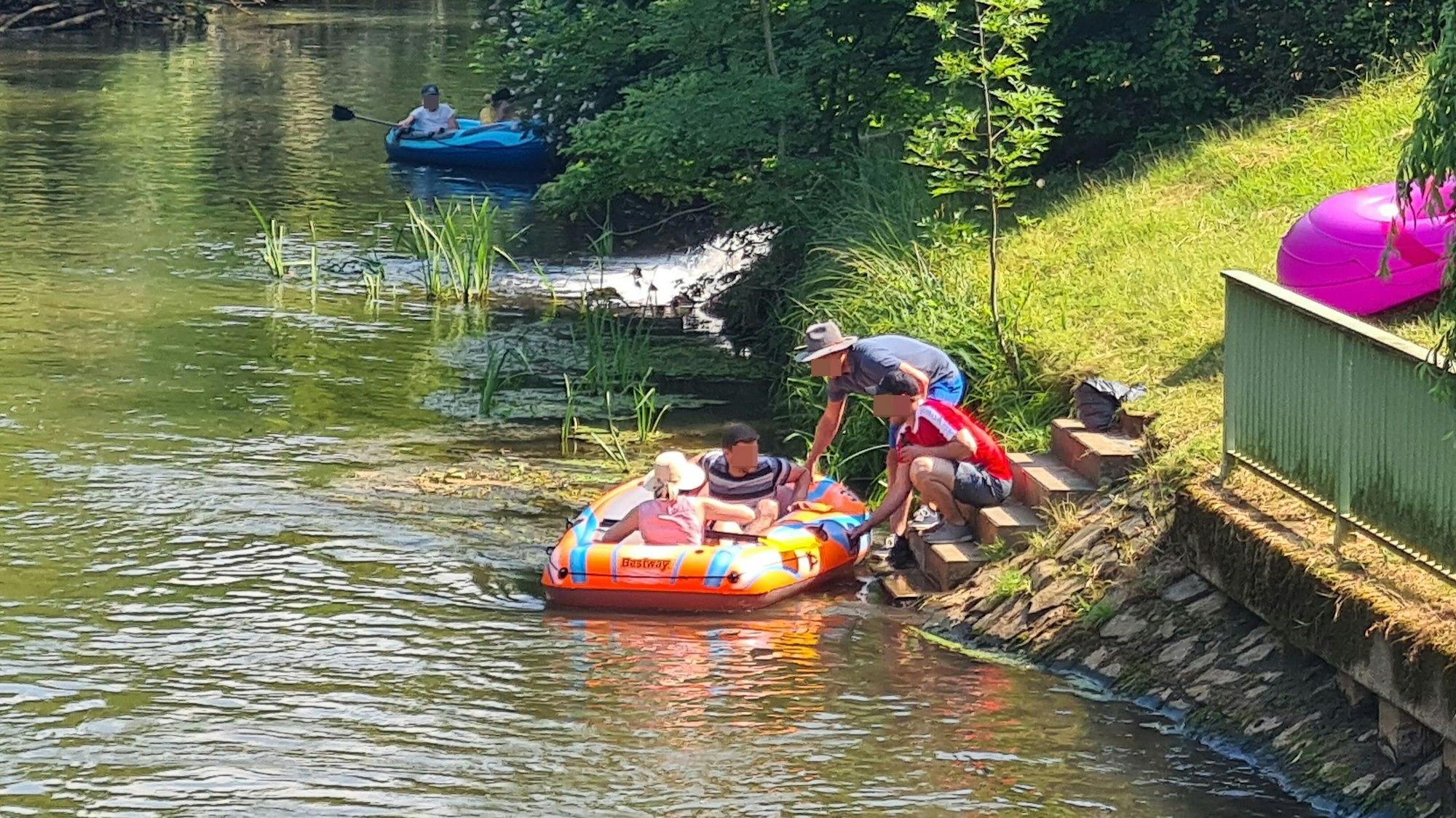 Das Bild zeigt zwei Kinder in einem Schlauchboot auf der Erft. Am Ufer hocken zwei Erwachsene, die das Schlauchboot festhalten.