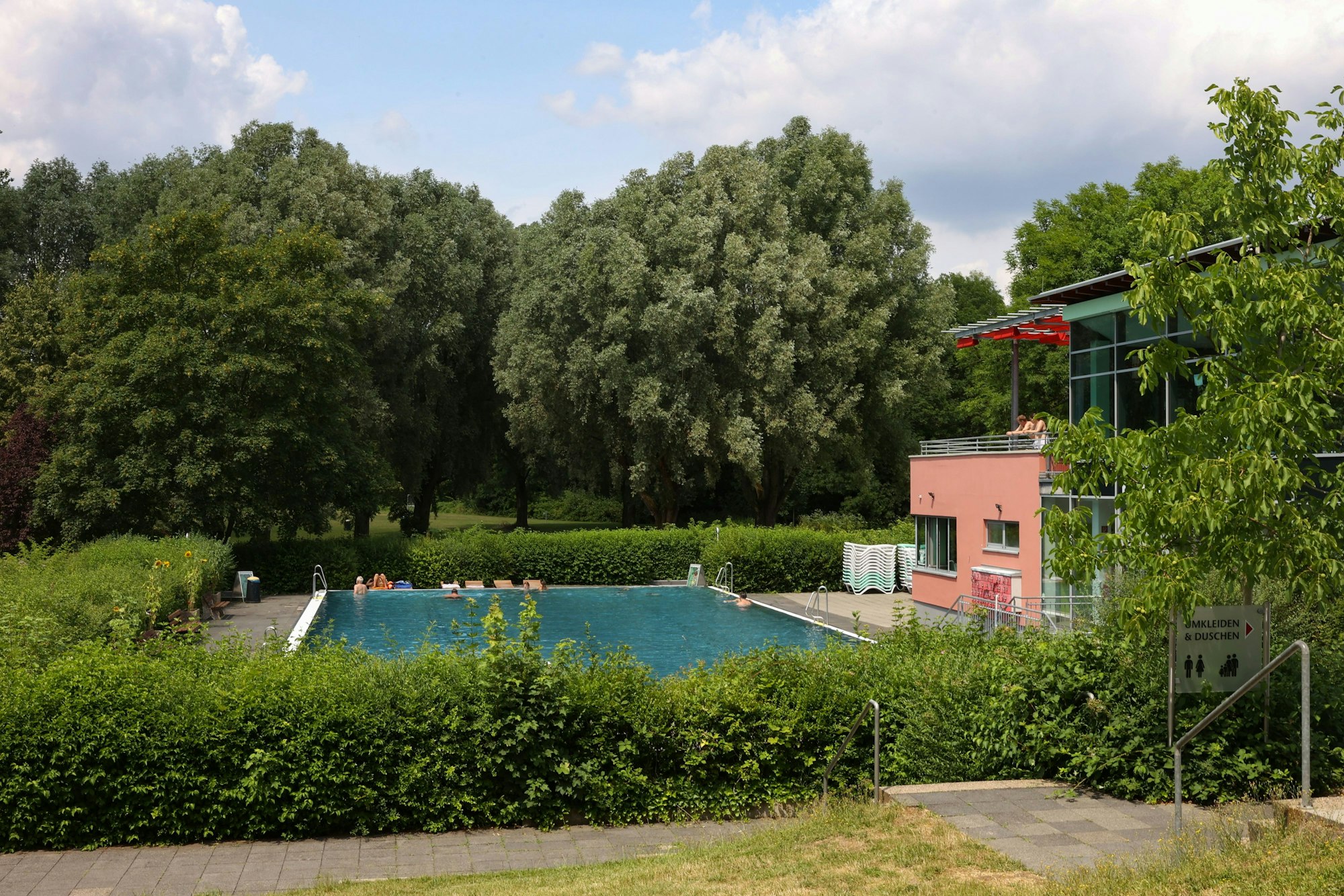 Das Bild zeigt das große Nichtschwimmerbecken im Zündorfbad, das eingerahmt von Bäumen ist.