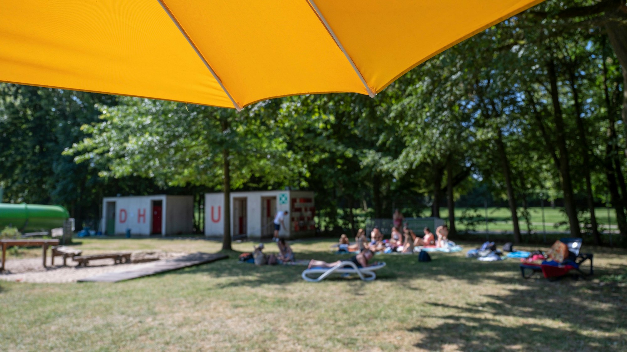 Ein Sonnenschirm mit der Liegewiese des Ossendorfbads, sowie den Sanitätsanlagen im Hintergrund
