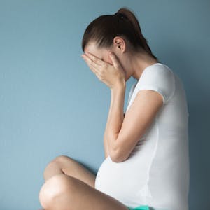 Eine gestresste schwangere Frau vor blauem Hintergrund.