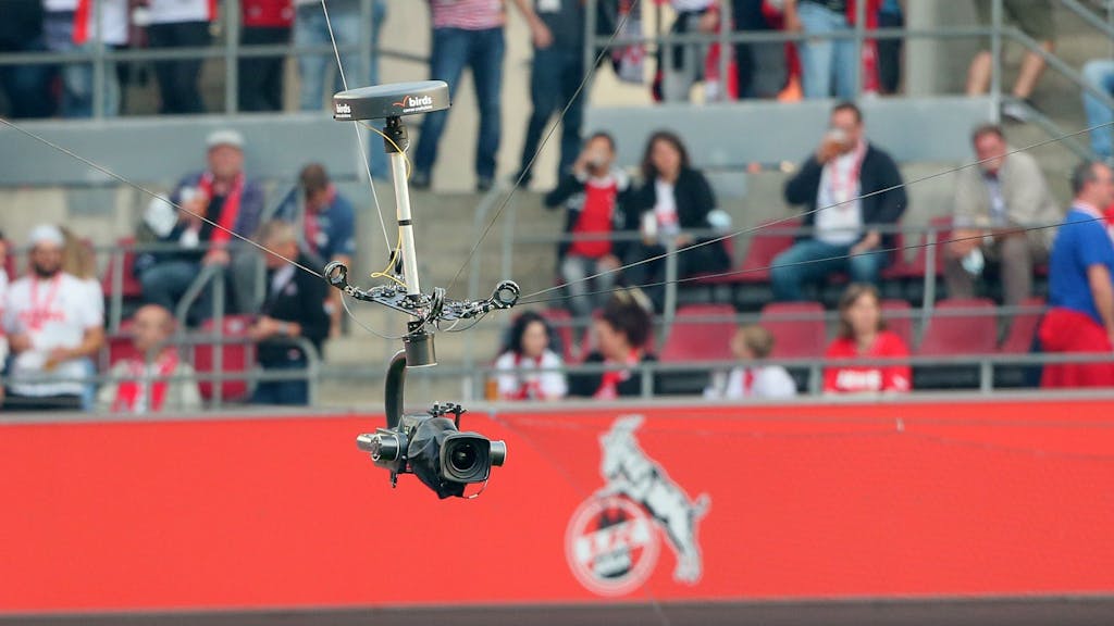 Eine Kamera schwebt im Rhein-Energie-Stadion. Im Hintergrund sind Fans und das Logo des 1. FC Köln zu erkennen.