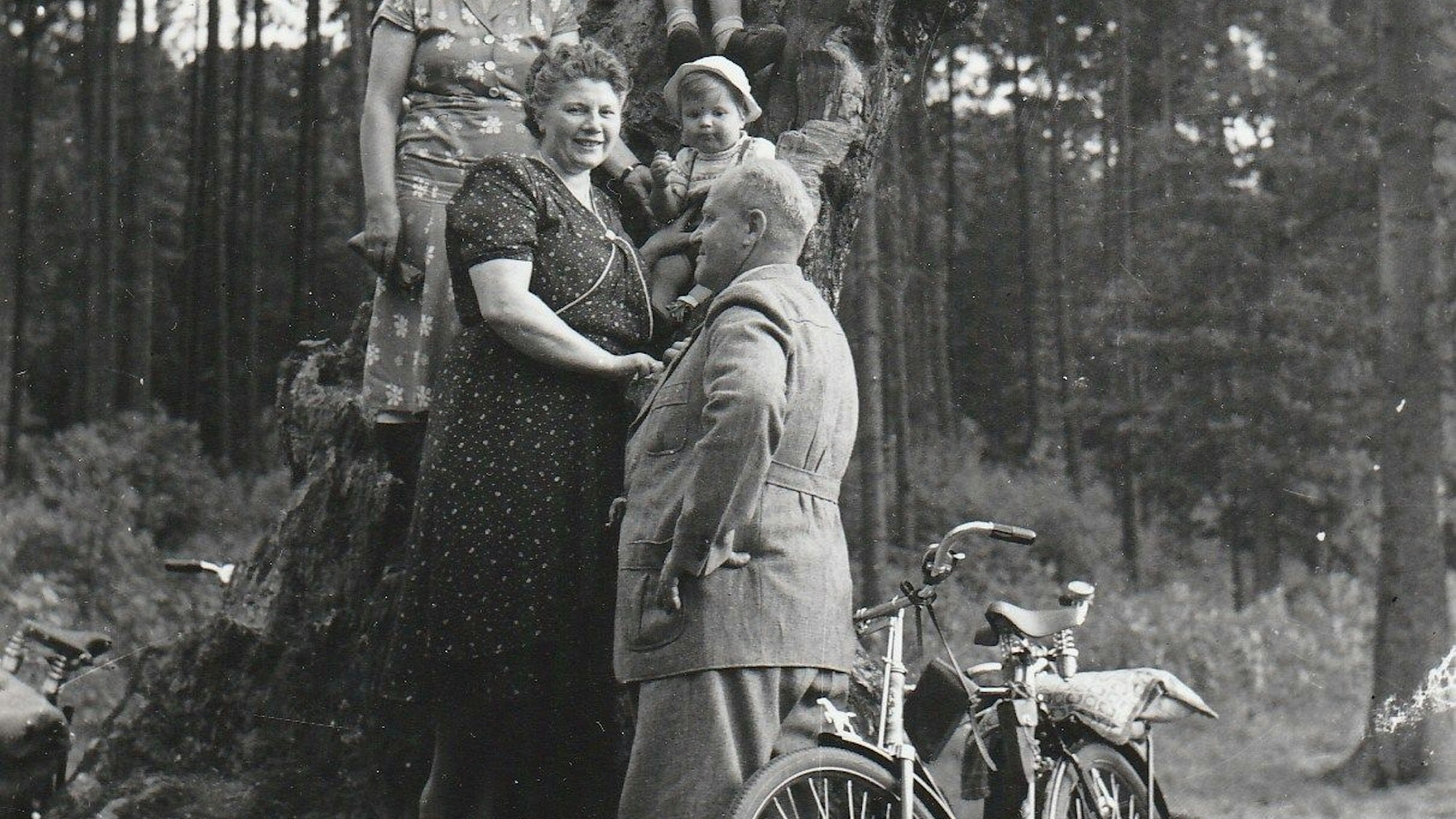 Schwarz/Weiß-Bild einer Familie, vorne ein altes Fahrrad, im Hintergrund ein Kölner Wald