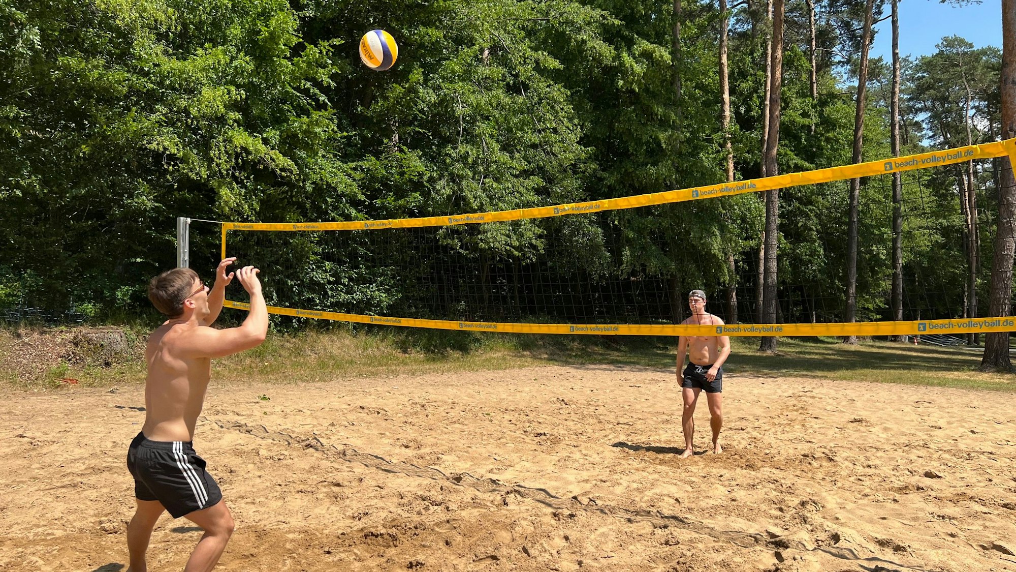 Zwei Männer spielen Beachvolleyball und werfen den Ball übers Netz.