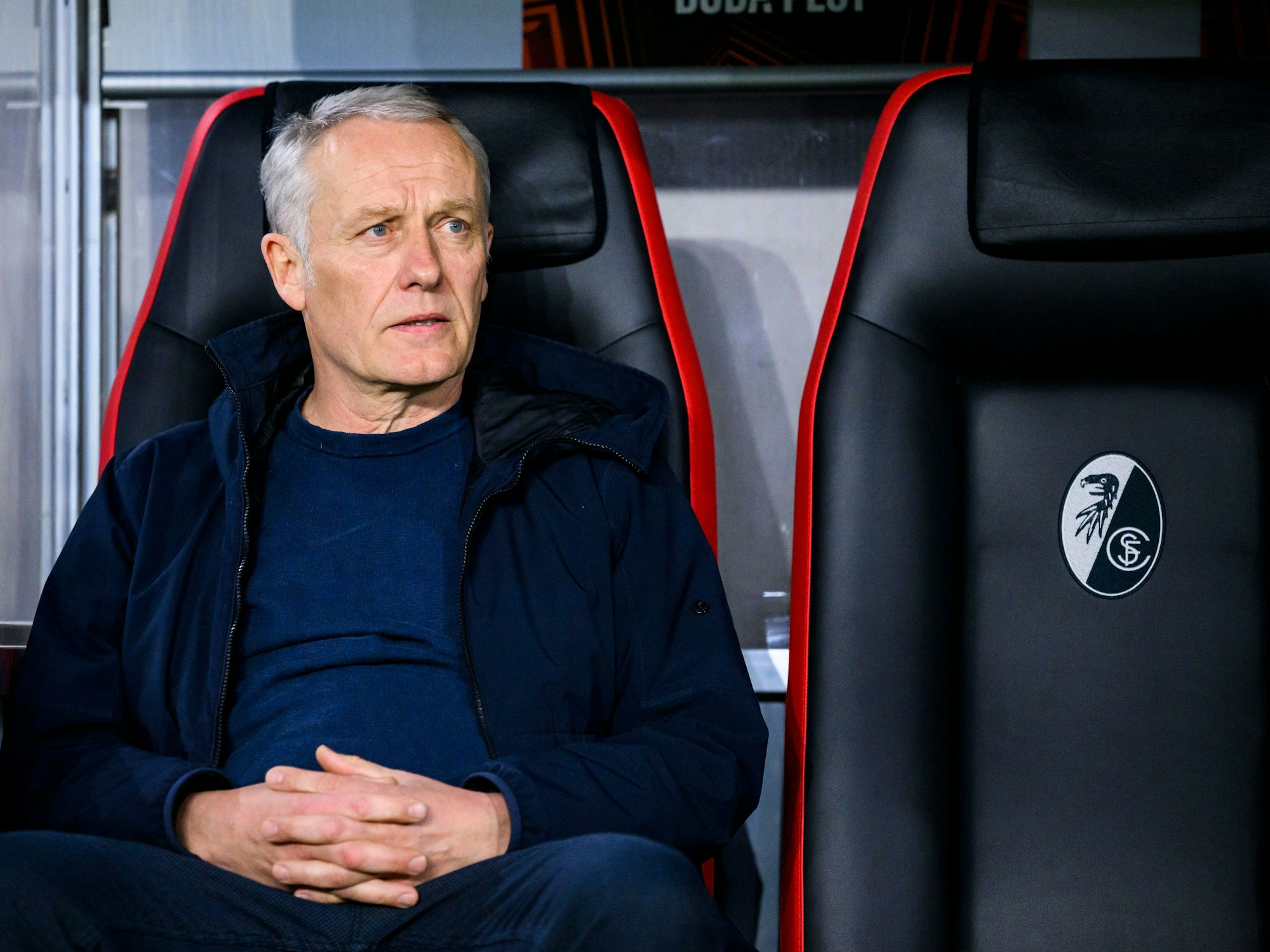 SC Freiburgs Trainer Christian Streich sitzt vor dem Spiel im Stadion auf der Trainerbank.