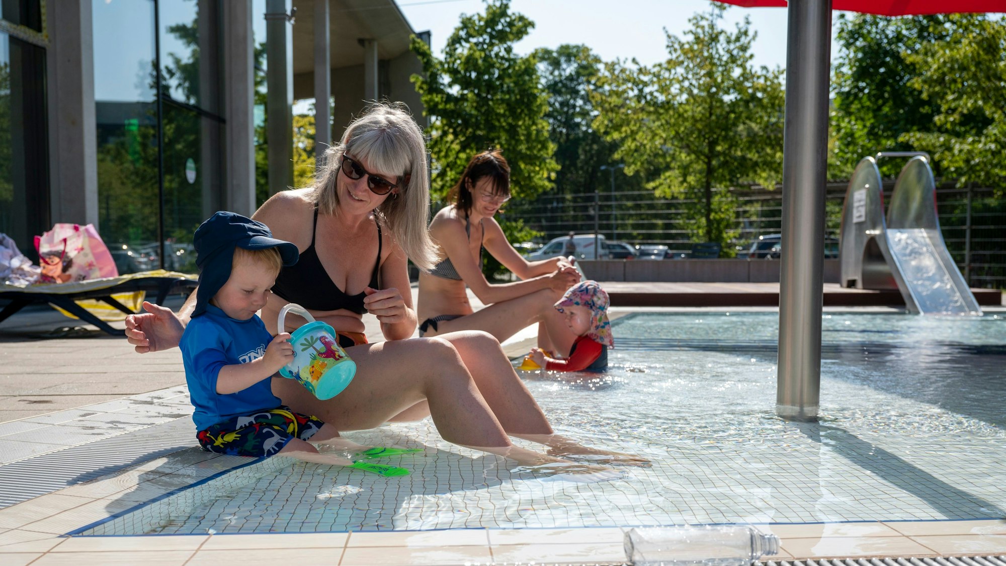 Zwei Frauen spielen mit ihren Kindern im Kinderschwimmbecken.