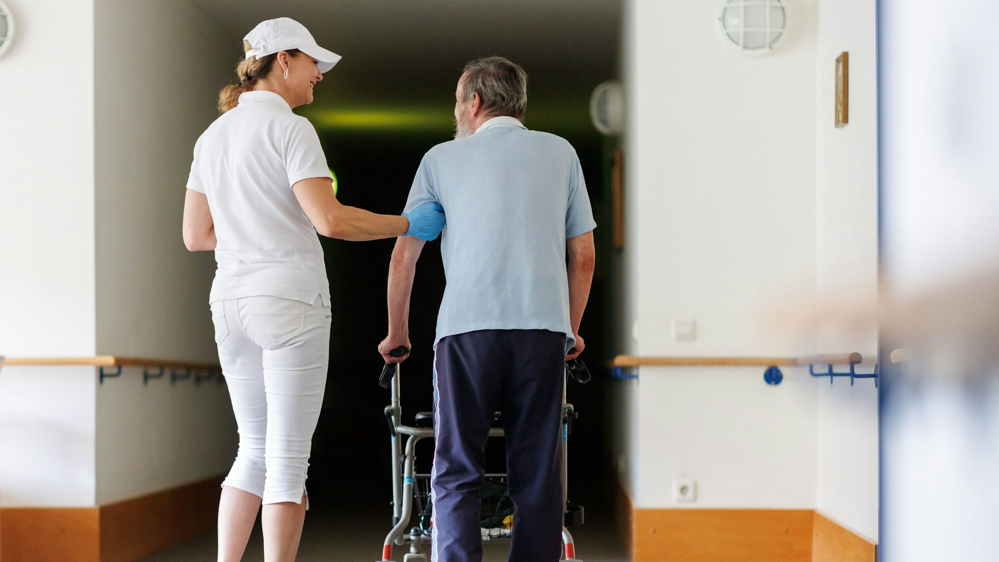 Svetlana (l.), ambulante Pflegefachkraft, begleitet einen Bewohner des Betreuten Wohnens mit seiner Gehhilfe durch das Gebäude. (Symbolbild)