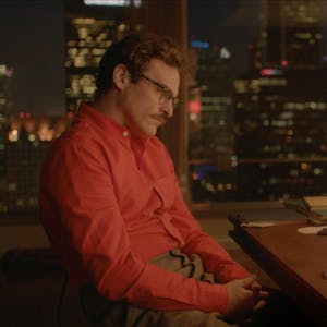 Joaquin Phoenix sitzt im Film „Her“ vor einem Computerbildschirm. Sein oranges Hemd korrespondiert mit dem orangen Hintergrundbild des Betriebssystems.&nbsp;