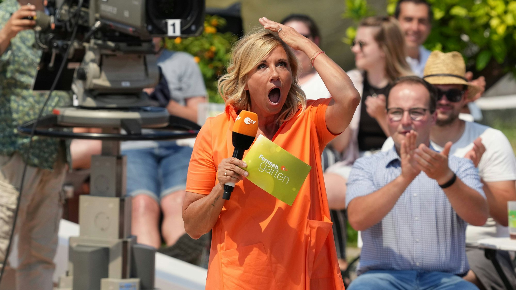 Das Foto zeigt Moderatorin Andrea Kiewel in der Kulisse des „Fernsehgarten“, wo sie sich entgeistert an den Kopf fasst. Es stammt aus der Show vom 25. Juni 2023.