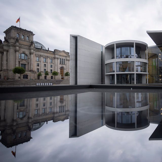 Das Paul-Löbe-Haus (M) des Deutschen Bundestages spiegelt sich neben dem Reichstagsgebäude (l) in einer Glasfläche.