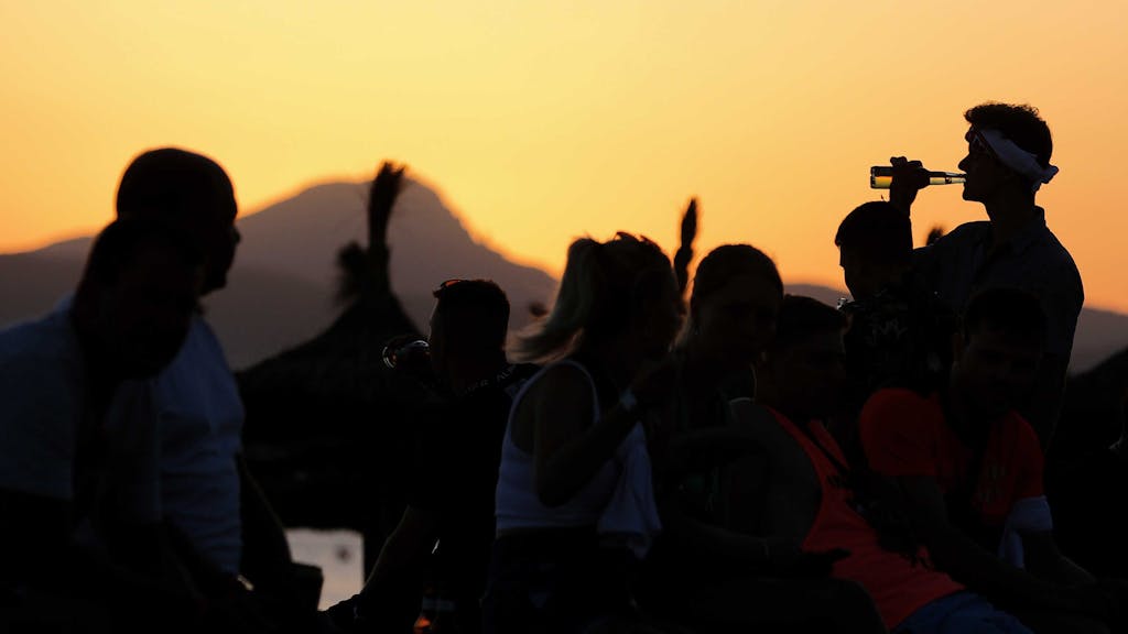 Vorwiegend junge Leute feiern bei Sonnenuntergang am Strand von Arenal am Party-Viertel Ballermann auf Mallorca.