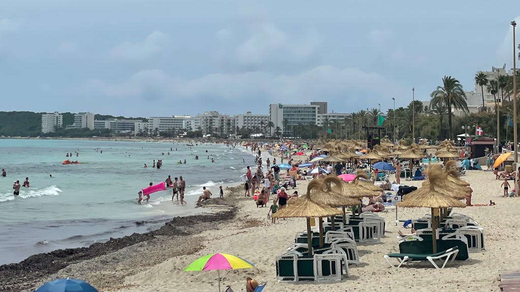 Urlauber und Urlauberinnen tummeln sich am Strand in Cala Millor auf Mallorca.