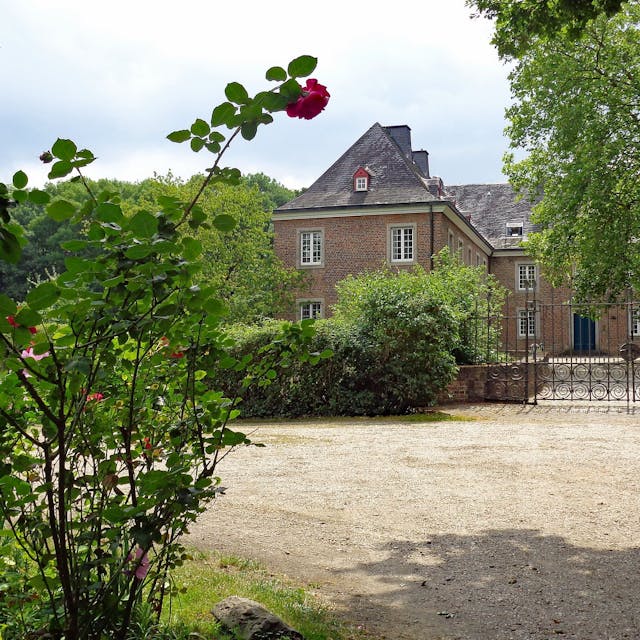 Die Burg Bachem in Frechen, umgeben von Grün und Rosenbüschen.