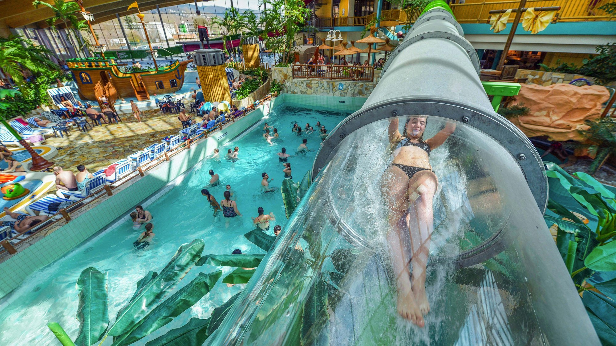 ein Mädchen rutscht durch eine transparente Wasserrutsche in einem Spaßbad