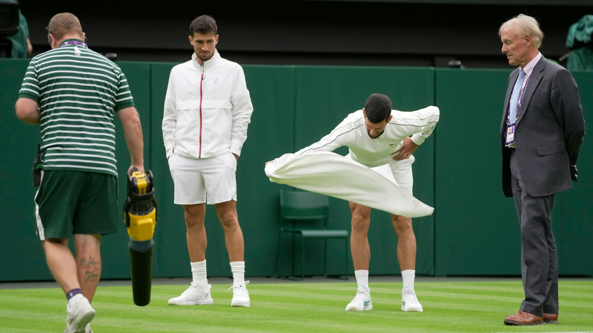 Novak Djokovic versucht, den Rasen auf dem Centre Court mit einem Handtuch-Wirbel zu trocknen.