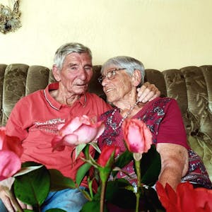 Margret und Bernd Keßenich aus Weilerswist sitzen auf einer Couch und halten sich im Arm. Im Vordergrund sind Rosen.