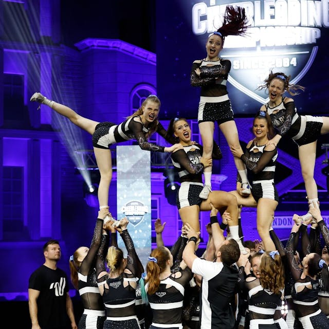 Ein Cheerleader-Team steht als menschliche Pyramide auf der Bühne.
