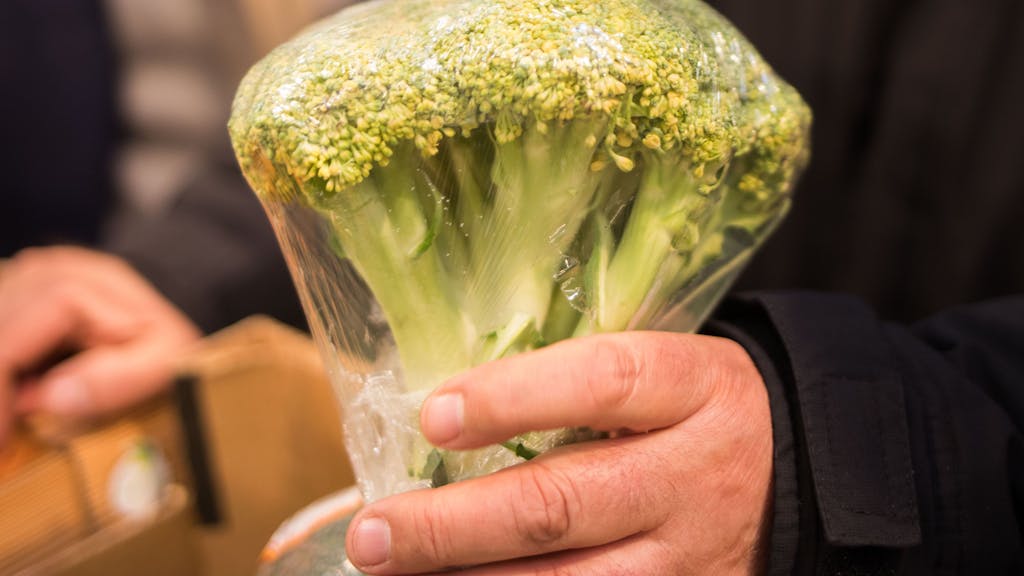 Eine Person hält einen in Plastik verpackten Broccoli.