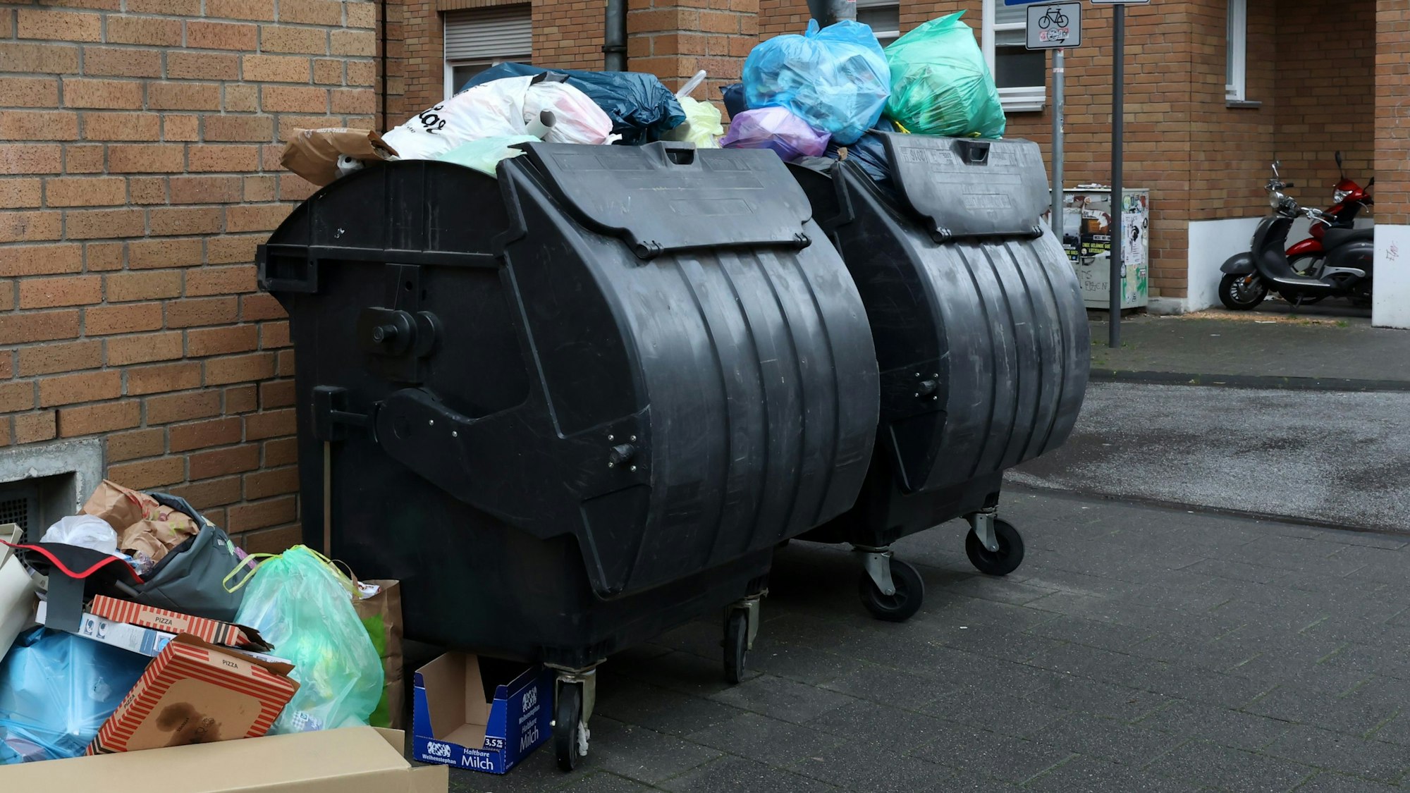 Volle Abfallgroßbehälter stehen in Köln an der Straße.
