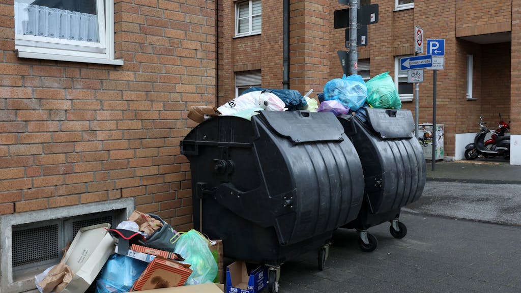 Volle Mülltonnen stehen vor einem Wohnhaus in Köln.
