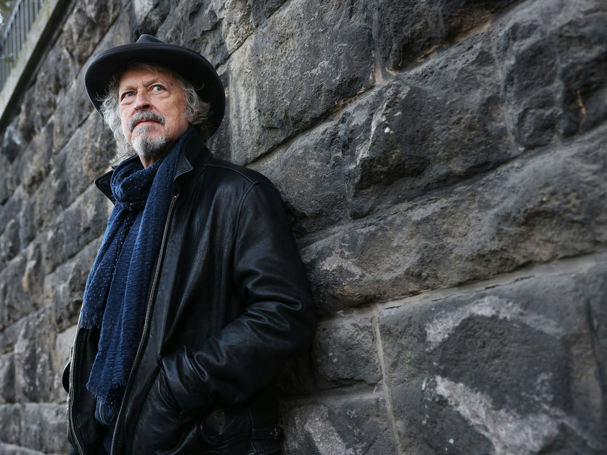 Wolfgang Niedecken, Musiker und Sänger, steht am Straßenrand angelehnt an einer Mauer.
