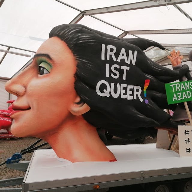 Der Woman-Life-Freedom-Wagen auf dem Kölner CSD wurde von Jaques Tilly gebaut. Vorne wird ein Kunstwerk einer Frau sein, die mit ihren Haaren einen Mullah erwürgt. Zusätzlich steht "Iran ist queer!" in ihren Haaren. Auf einem grünen Schild steht außerdme „Trans Azadi“, auf einem weiteren „#Women #Life #Freedom“.