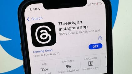 Die Ankündigung der Social-Media-App Threads wird im US-amerikanischen App Store von Apple angezeigt. Im Hintergrund ist das Twitter-Logo zu sehen.