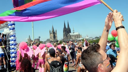 Jemand schwingt eine Regenbogenflagge. Im Hintergrund ist der Kölner Dom zusehen.