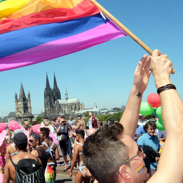 Jemand schwingt eine Regenbogenflagge. Im Hintergrund ist der Kölner Dom zusehen.