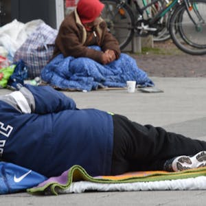 Das Foto zeigt einen obdachlosen Menschen, der auf dem Asphalt liegt.