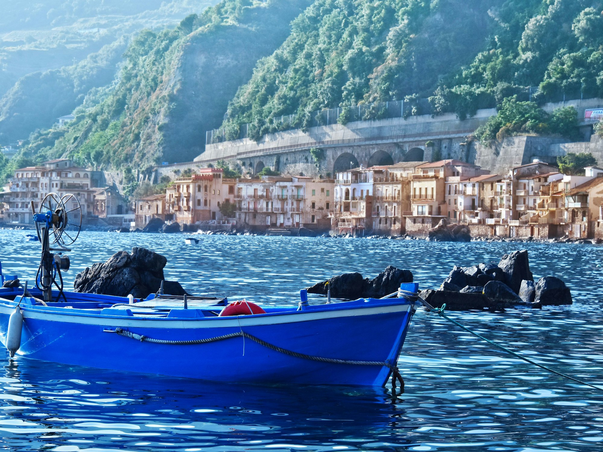 Ein blaues Fischerboot schwimmt auf dem Wasser vor der malerischen Küste von Scilla, Italien.