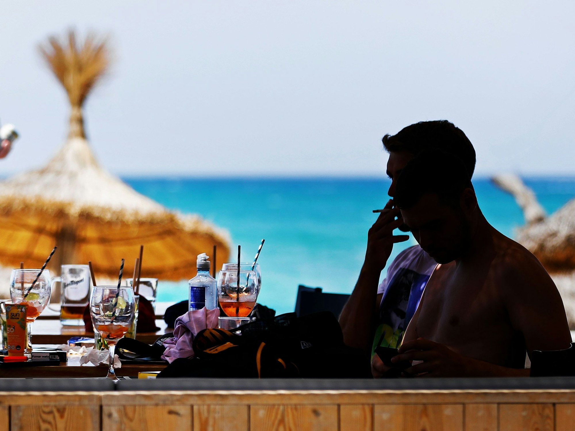 Junge Männer sitzen an der Strandpromenade amStrand von Arenal auf Mallorca in einer Bar und trinken und rauchen.