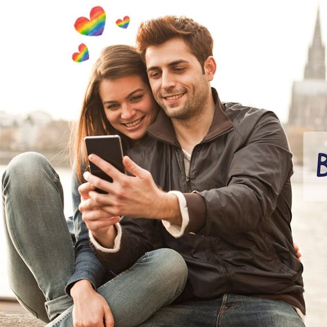 Eine Frau und ein Mann stehen auf der Rheinpromenade mit dem Kölner Dom und der Hohenzollernbrücke im Hintergrund und schauen lächelnd auf ein Smartphone. Daneben das Logo der Website Bütz mich.