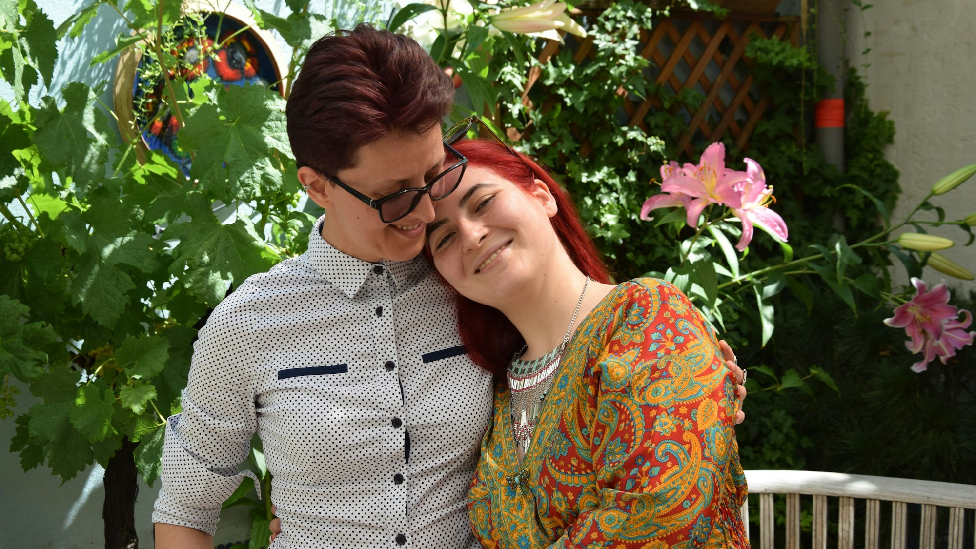 Adina Lupu (rechts) und Valeria Gavrilă stehen vor einem Hintergrund aus Pflanzen. Gavrilă lehnt an Lupus Schulter, lächelt in die Kamera. Lupu schaut sie an.