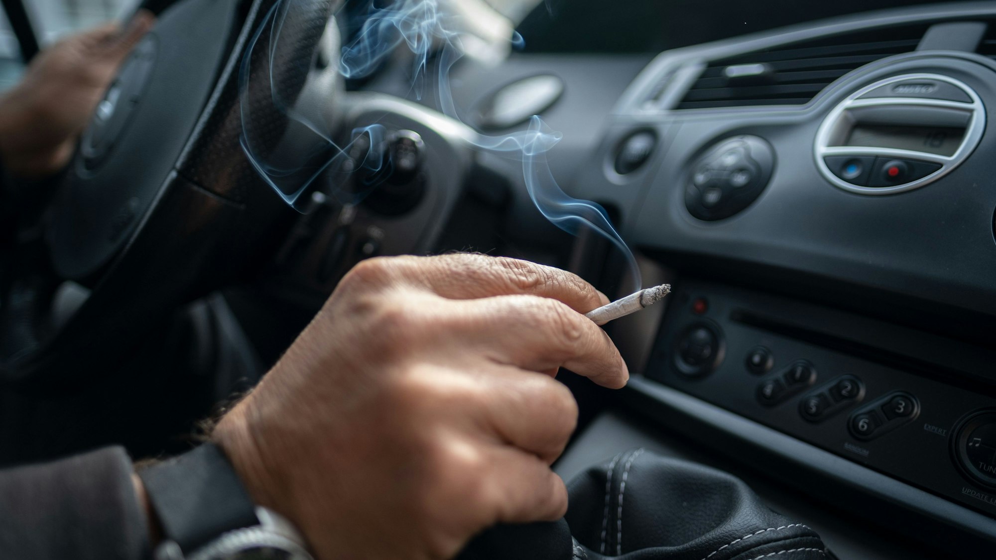 Ein Mann sitzt rauchend am Lenkrad eines Autos. (Symbolbild)