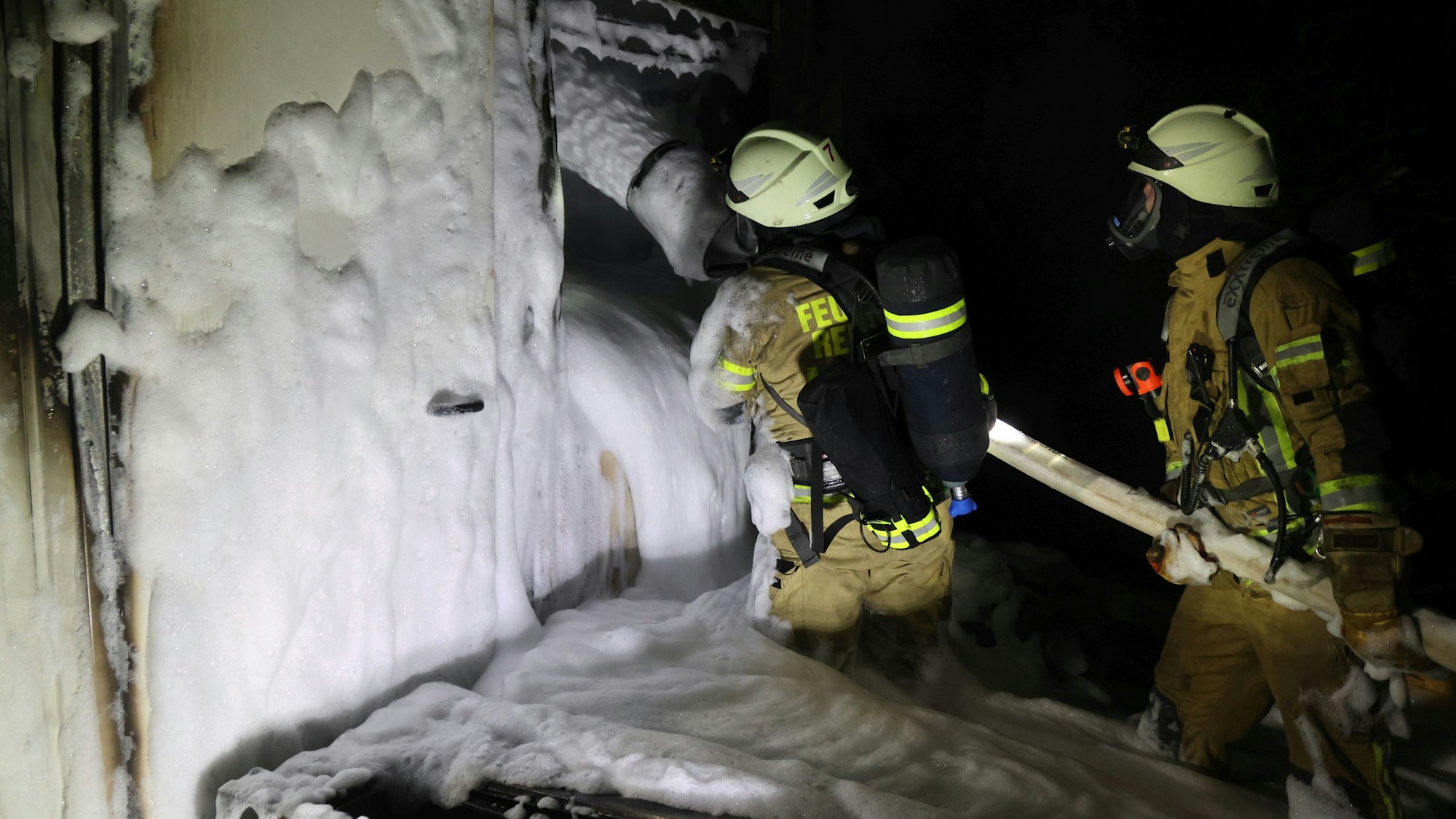 Zwei Feuerwehrleute füllen Schaum aus einem Schlauch in einen Wohncontainer.