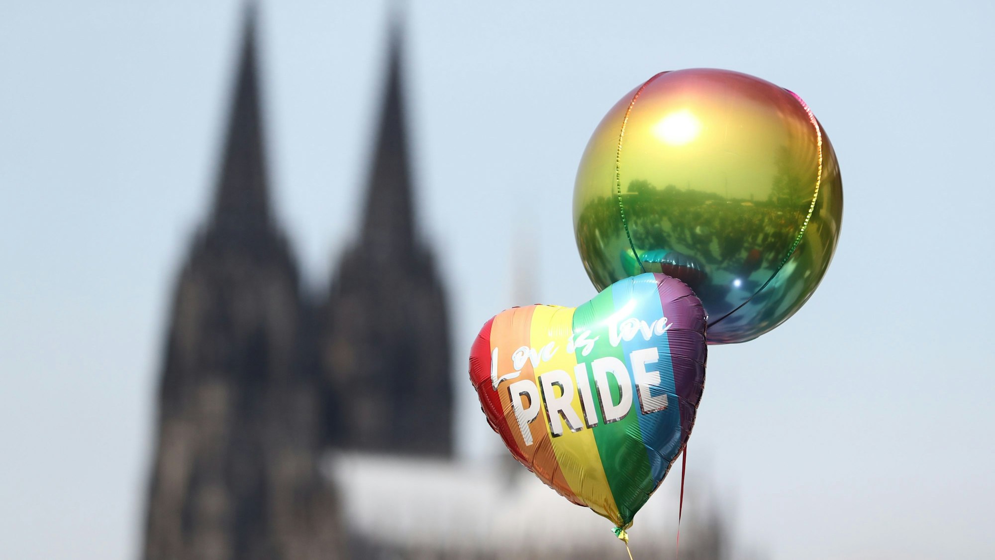 Zwei Regenbogen-Luftballons fliegen vor dem Dom. Auf dem einen herzförmigen steht „Love ist Love. Pride“ (Liebe ist Liebe. Stolz) in weißer Schrift.