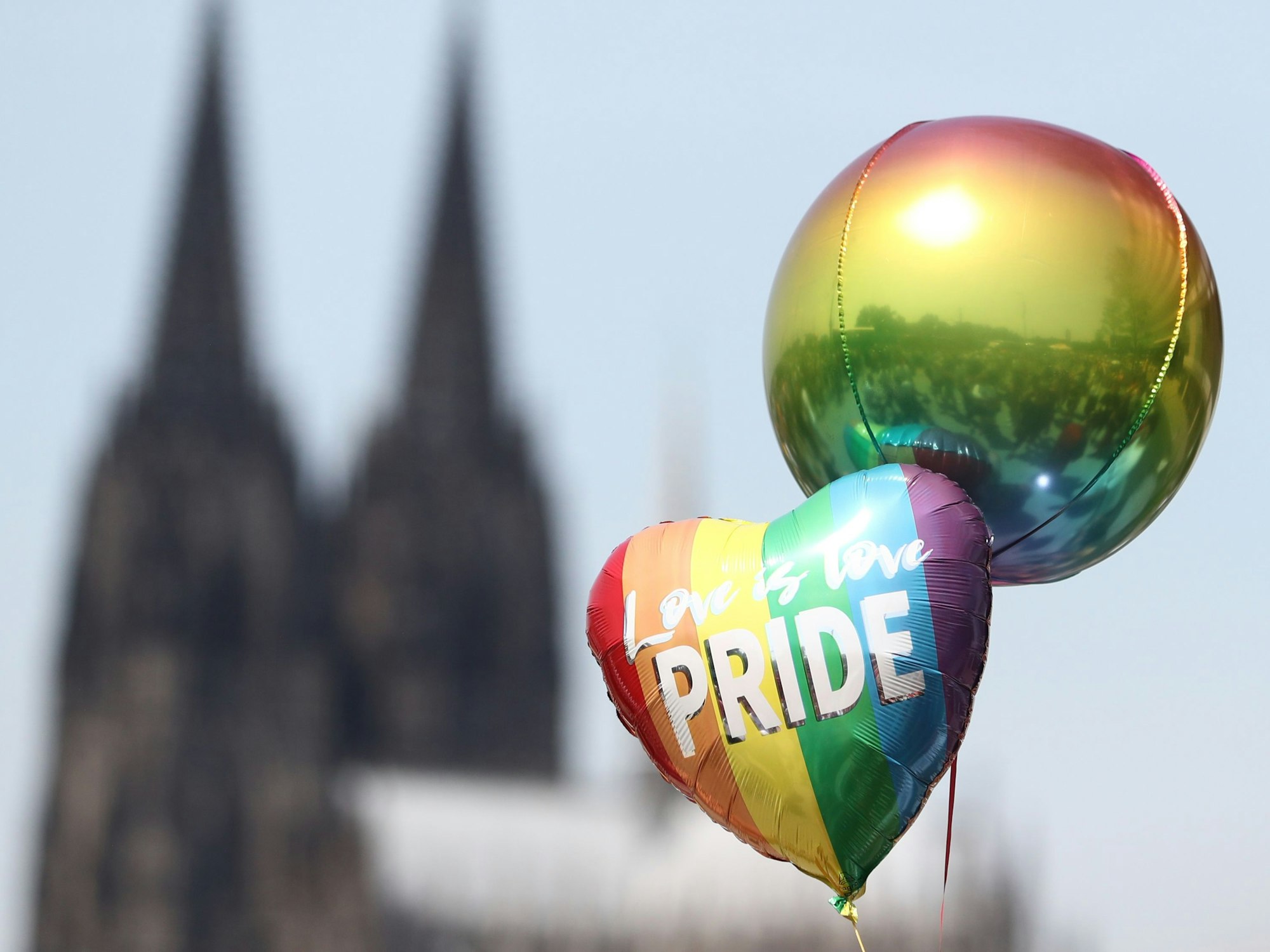 Zwei Luftballons in Regenbogenfarben. Im Hintergrund der Kölner Dom.