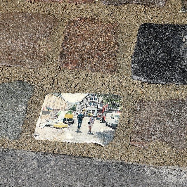 Das Bild zeigt mehrere Pflastersteine in Bad Münstereifel. Der Mittlere ist mit einem Motiv aus den Tagen nach der Flutkatastrophe bedruckt.&nbsp;