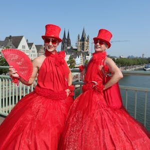Zwei in Rot gekleidete Teilnehmende an der CSD-Parade stehen auf der Deutzer Brücke