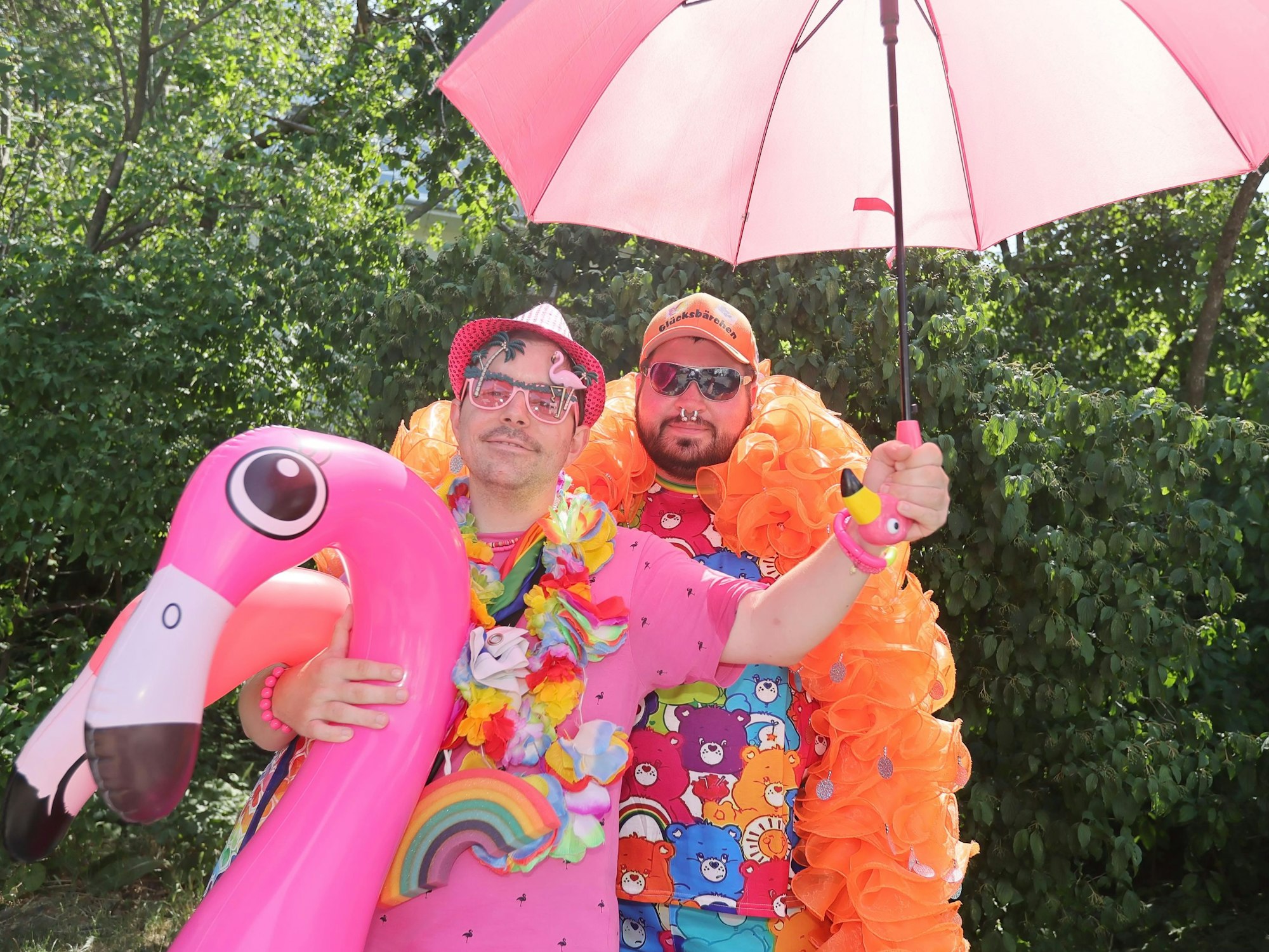 Zwei Menschen posieren zusammen. Sie haben einen aufblasbaren Flamingo, einen pinken Sonnenschirm an.