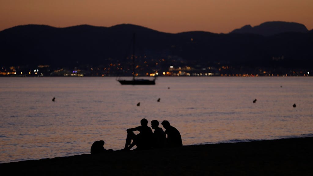 Vier Personen sitzen nach Sonnenuntergang am Strand von Palma de Mallorca.