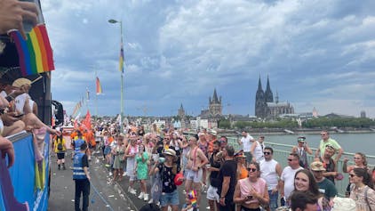 Dicht gedrängt stehen Menschen auf der Deutzer Brücke und schauen die vorbeiziehenden Wagen der CSD-Parade in Köln im Juli 2023 an.