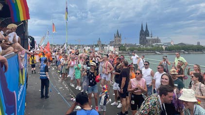Dicht gedrängt stehen Menschen auf der Deutzer Brücke und schauen die vorbeiziehenden Wagen der CSD-Parade in Köln im Juli 2023 an.