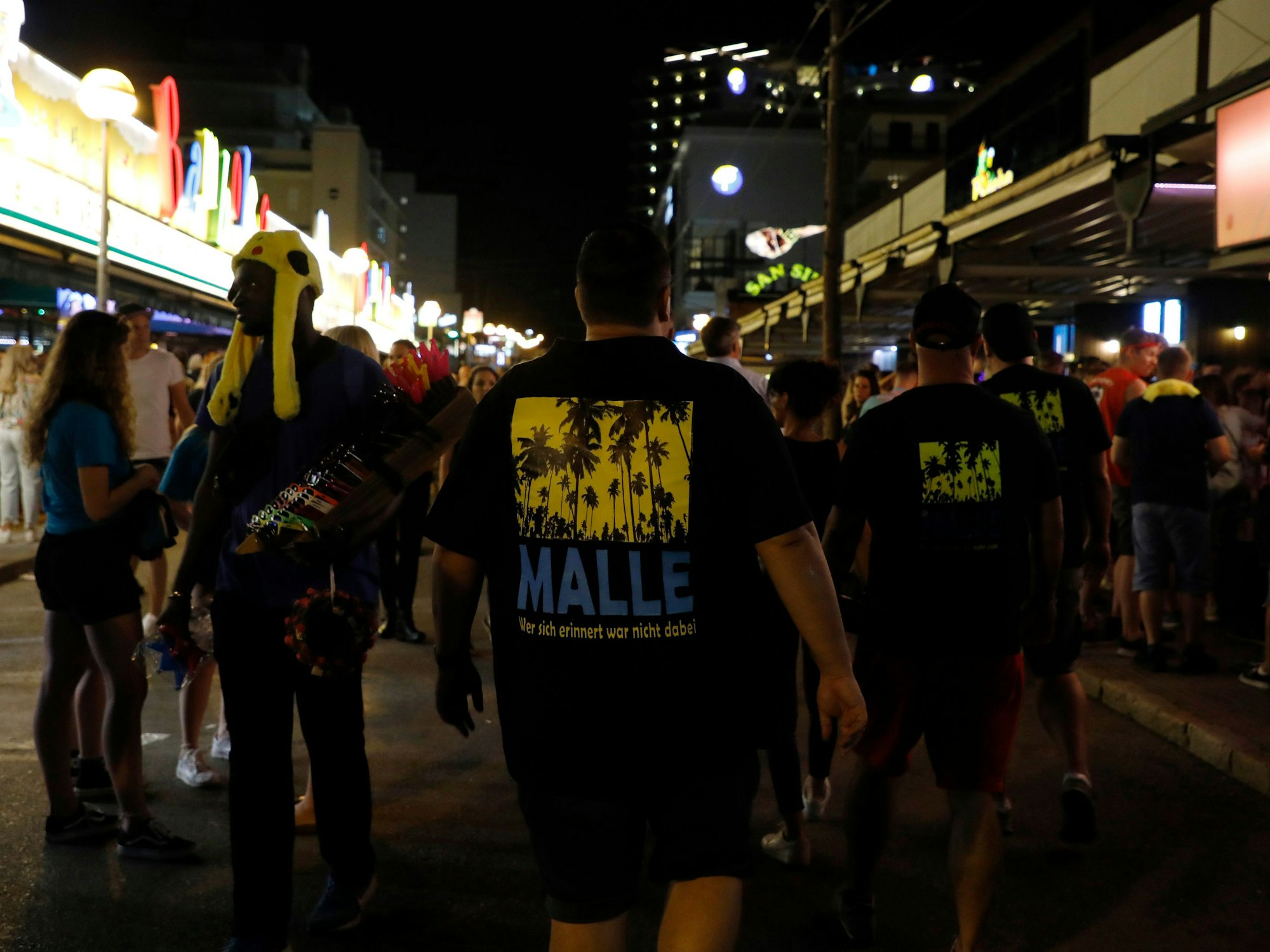 Männer, die ein T-Shirt mit der Aufschrift „Malle“ tragen, gehen am 27. Mai 2023 durch die Schinkenstraße am Ballermann auf Mallorca.